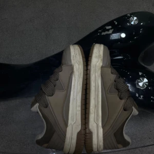 Bruna sneakers med breda snören - Säljer ett par bruna sneakers med breda snören och robust sula. Skorna har en låg profil och är tillverkade i en kombination av textil och syntetmaterial. Lite smuts på sulan men går enkelt att tvätt med sko puts pris kan diskuteras.Skorna är i storlek 41 