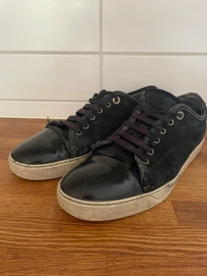 Lanvin  - Säljer ett par svarta sneakers med snygga lackade tåpartier och mockaliknande material på sidorna. Skorna har svarta skosnören. Perfekta för dig som gillar en stilren men ändå edgy look.