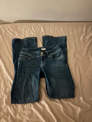 Blå bootcut jeans med broderade fickor - Säljer ett par klassiska blå bootcut jeans med snygga broderade detaljer på bakfickorna. Jeansen har låg midja, fem fickor och stängs med dragkedja och knapp. Perfekta för en avslappnad och trendig look, kommer inte till användning längre, innerbensmåttet är 80💕