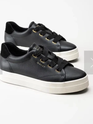 Svarta GANT sneakers i läder - Stilrena svarta sneakers från GANT i slätt läder med breda svarta skosnören och guldfärgade öljetter. Klassisk låg modell med vit sula och diskret GANT-logga på sidan. Perfekta för en clean och modern look.