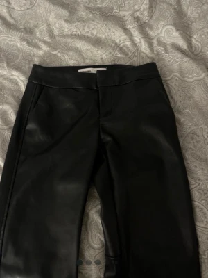Svarta fuskskinnbyxor från Bershka - Snygga svarta byxor i fuskskinn från Bershka. Bootcut, medel  midja och diskreta fickor på sidorna. Perfekta för dig som vill ha en edgy och trendig look. Materialet är glansigt och ger en cool känsla till outfiten. Jätte fint skick. Har sytt upp de så de passar en som är ca 160-163. Lägg ett bud!!