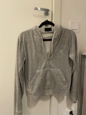 Grå zip hoodie med huva juciy  - Säljer en enkel och stilren grå hoodie med dragkedja framtill och två stora fickor. Hoodien har justerbar huva med snören och är tillverkad i mjukt sweatshirtmaterial. Perfekt för en avslappnad look.