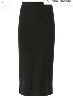 Svart ribbad pennkjol från Pieces - Svart pennkjol från Pieces med ribbad struktur och elastisk midja. Kjolen är knälång och har en liten slits på sidan för extra rörelsefrihet. Perfekt för dig som gillar en enkel och stilren look.