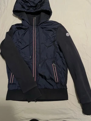 100% äkta Moncler cardigan i mjukt tyg - En enkel svart cardiganjacka i mjukt tyg. Rak passform med långa ärmar och diskret design utan synliga detaljer. Perfekt att slänga på sig över en t-shirt eller topp för en clean look. Köptes på vinted med äkthetsverigiering som godkändes. Vinns lite slitage på den som man kan se på bilder. Flexibel när det kommer till priset då jag vill bli av med den