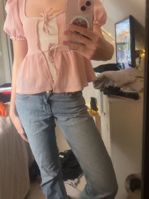 Ljusrosa blus med knyt framtill - Supersöt ljusrosa blus med puffärmar och två knyt framtill. Blusen har en luftig och flowy passform med lätt rynkat tyg som ger en romantisk vibe. Perfekt att styla med jeans eller kjol för en trendig look.🩷🩷🌷