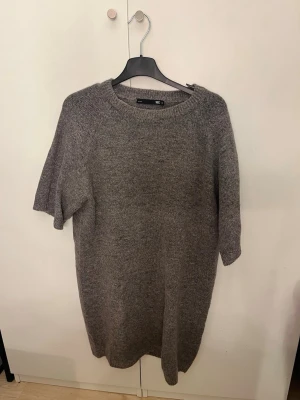 Grå stickad klänning från H&M - Mysig grå stickad klänning från lager 157 med rund halsringning och halvlånga ärmar. Perfekt för lager på lager och enkel att styla med boots eller sneakers. Materialet känns mjukt och bekvämt, och modellen är rak och avslappnad. Finns en liten fläck på nederkanten av klänningen, men inget som syns