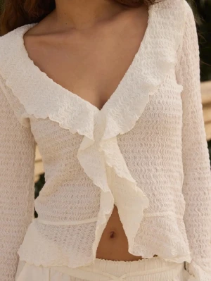 Vit volangblus med v-ringning från Nelly - Slutsåld vit/krämvit blus med långärmad design, djup v-ringning och volangdetaljer längs halsringningen och framtill, storlek xs (passar även S) Blusen har ett vågigt, strukturerat tyg och utsvängda ärmslut som ger en romantisk vibe. Nästan aldrig använd och perfekt att styla med jeans eller kjol! 💕