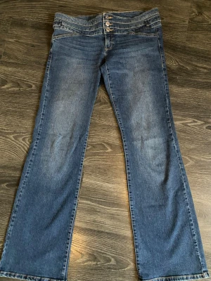Blå bootcut jeans med tredubbel knapp - Säljer ett par blå bootcut jeans med låg midja. Det är  snygg tvätt och tredubbel knappstängning i midjan. Supersnygga och unika jesns. 