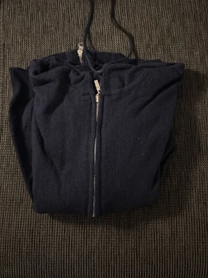 Mörkblå cashmere hoodie - Säljer en enkel och stilren mörkblå hoodie med dragkedja framtill och justerbar huva. Hoodien är tillverkad i mjukt bomullsliknande material och har långa ärmar. Perfekt för dig som gillar en clean och avslappnad look. 