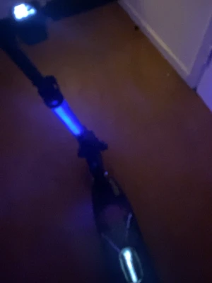 Elsparkcykel med LED-ljus - Säljer en elsparkcykel med svart ram och färgglad platta med geometriskt mönster. Utrustad med LED-ljus framtill och längs stången som lyser blått. Perfekt för att ta sig runt snabbt och smidigt. Laddas enkelt och har bekväma handtag.