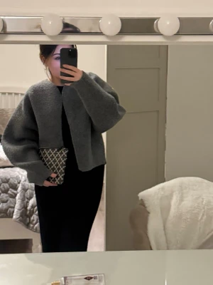 Grå oversized stickad kofta - Mysig grå stickad kofta med oversized passform och ballongärmar. Koftan har en enkel, öppen design utan knappar och är tillverkad i ett grovt, mjukt material som ger en avslappnad look. Perfekt att slänga på sig över en t-shirt eller topp.