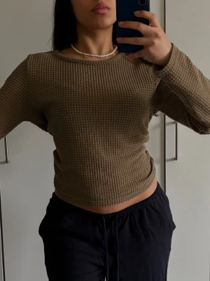 Beige croppad stickad tröja - Säljer en beige croppad stickad tröja med lång ärm och grov, rutmönstrad struktur. Tröjan har rund halsringning och är tillverkad i ett mjukt, stretchigt material som känns skönt mot huden. Perfekt för lager på lager och enkel att styla till olika outfits.