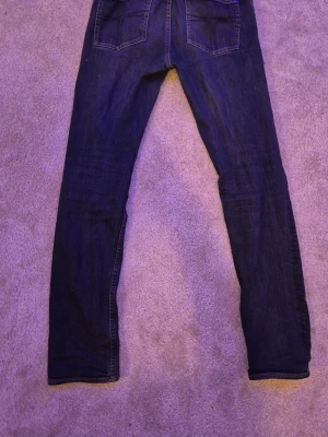Mörkblå slim fit jeans - Säljer ett par mörkblå slim fit jeans med klassisk femficksdesign och raka ben. Jeansen har snygga kontrastsömmar och är tillverkade i mjukt denimtyg som sitter skönt. Perfekta för dig som gillar en enkel och stilren look.