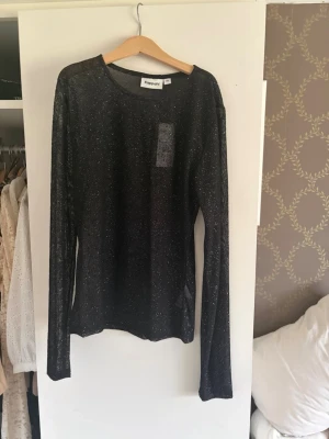 Svart glittrig topp från Kappahl - Snygg svart långärmad topp från Kappahl med glittrigt material. Tunn och lätt, perfekt för att addera lite extra till din outfit. Rund halsringning och figurnära passform. Aldrig använd 