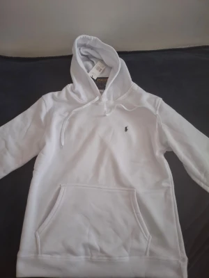 Vit hoodie från Polo Ralph Lauren - Snygg vit hoodie från Polo Ralph Lauren med klassisk huva och dragsnören. Tillverkad i mjukt material som känns skönt mot huden. Perfekt för en avslappnad och stilren look. L MEN PASSAR M