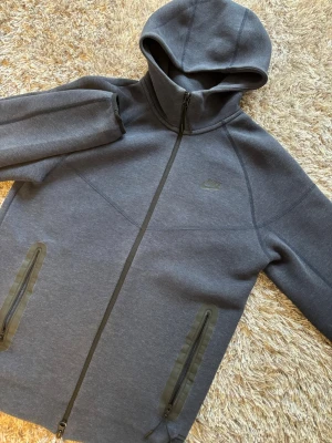 Mörkblå Nike tech  hoodie med dragkedja - Snygg mörkblå nike tech hoodie med hel dragkedja framtill och två fickor med dragkedja. Hoodien har en stilren design med diskret Nike-logga på bröstet och en skön huva. Perfekt för dig som gillar sportig och avslappnad stil.