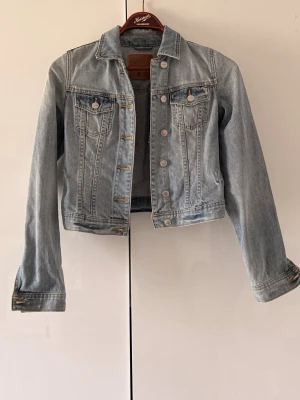 Ljusblå jeansjacka (Gina Tricot) - Snygg ljusblå jeansjacka från g perfect jeans med klassisk krage, två bröstfickor med lock och knappar framtill. Jackan har raka ärmar och kontrastsömmar som ger en tidlös look. Perfekt att slänga över en hoodie eller t-shirt.