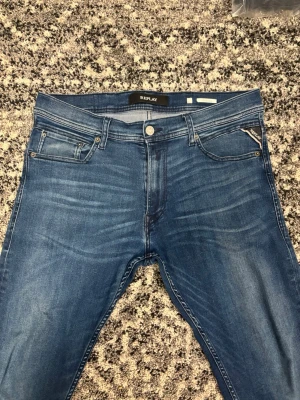 Blå Replay jeans med tvättade detaljer - Snygga blå jeans från Replay med klassisk femficksmodell och ljusa tvättade detaljer framtill. Jeansen har raka ben, normal midja och Replay-logga på bakfickan samt patch i läderimitation bak. Materialet är mjukt denim som ger en bekväm känsla. Byxorna passar i storlekarna 32/32 och i 30/32. Hör av er vid eventuell frågor eller funderingar!!