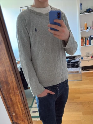 Grå tröja från Polo Ralph Lauren - Snygg och enkel grå långärmad tröja från Polo Ralph Lauren. Tillverkad i mjukt material med rund halsringning och klassisk passform. Perfekt basplagg för en clean och stilren look.
