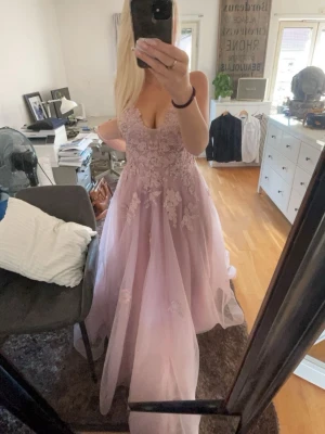 Ljusrosa balklänning - Säljer min ljusrosa balklänning med vackra spetsapplikationer och blommiga detaljer. Klänningen har djup urringning, öppen rygg med snörning och tunna axelband som korsas i ryggen. Tyvärr har en pad lossnat längst ner men går lätt att sy fast med nål och tråd. Lite smutsig längst ner på under tygget men inget som syns.💞