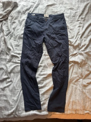 Mörkblå chinos från Dressman - Snygga mörkblå chinos från Dressman med slim passform och knappgylf. Byxorna har sidofickor och är tillverkade i ett mjukt bomullsmaterial som ger en stilren look. Perfekta för en avslappnad men ändå uppklädd stil. Byxorna är helt oanvända