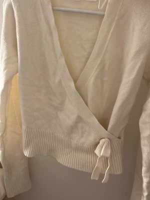 Vit omlottstickad tröja Gina Tricot - Säljer en vit omlottstickad tröja från Gina Tricot. Tröjan har långa ärmar, bred ribbad mudd nedtill och knytband i sidan. Perfekt för lager på lager och ger en snygg siluett. Materialet är mjukt och bekvämt.