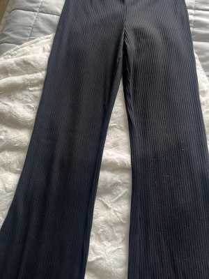 Svarta ribbade leggings med utsvängda ben - Säljer ett par svarta leggings med ribbad struktur och utsvängda ben. De är stretchiga och sitter skönt på kroppen. Perfekta för dig som gillar en enkel men trendig look. Materialet känns mjukt och följsamt.