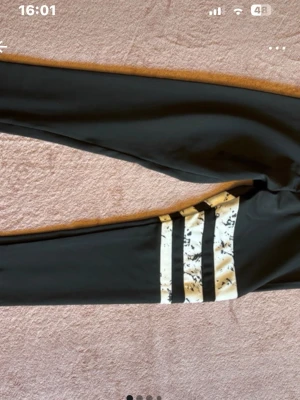Svarta leggings med vita marmor-ränder - Säljer ett par svarta leggings med tre vita ränder med marmormönster på ena benet. Tight passform och stretchigt material som passar perfekt till träning eller chill. Snygg kontrast mellan svart tyg och de vita detaljerna.