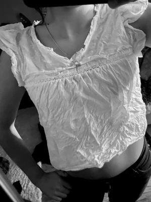 Vit blus med volangärmar - Söt vit blus med volangdetaljer vid axlarna och lätt rynkad struktur. Blusen har en lös passform och är något croppad. Perfekt för dig som gillar romantisk och luftig stil.