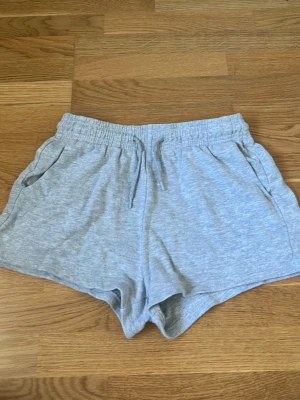 Grå mjuka shorts med snörning - Lätta och bekväma grå shorts med elastisk midja och snörning framtill. Shortsen har två sidofickor och är tillverkade i mjukt bomullsmaterial. Perfekta för varma dagar eller chill hemma.