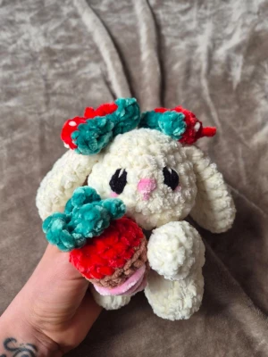 Virkad kanin med jordgubbe - Supergullig handvirkad kanin i mjukt, fluffigt garn. Kaninen är vit med långa öron, svarta ögon och rosa nos. Den har en stor röd och grön rosett på huvudet och håller i en virkad jordgubbe. Perfekt som dekoration eller present. ♡20cm lång