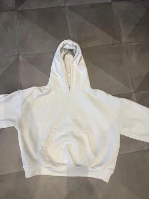 Vit hoodie  - Snygg vit hoodie med klassisk huva och stor magficka framtill. Tröjan har ribbade muddar vid ärmslut och nederkant, samt en avslappnad passform. Perfekt för en chill och stilren look. Materialet känns mjukt och bekvämt mot huden.