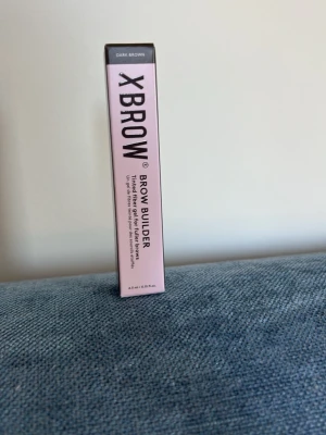 Xbrow Brow Builder Dark Brown - Xbrow Brow Builder i färgen Dark Brown. Ger fylligare och definierade ögonbryn med hjälp av bambufibrer, vitamin E och sötmandelolja. Kommer i en rosa och svart förpackning. Perfekt för att skapa naturligt snygga bryn.