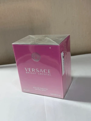 Versace Bright Crystal Eau de Toilette - Versace Bright Crystal Eau de Toilette i en snygg rosa och vit kartong. Parfymen kommer i en 90 ml förpackning och är känd för sin fräscha och blommiga doft. Perfekt för dig som gillar lyxiga och eleganta parfymer.