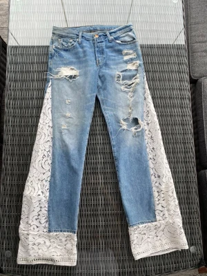 Blå jeans med vit spets och slitningar - Supersnygga och coola jeans som både är coola, söta och perfekta för våren och sommaren!💙Måtten är: innerbenslängd: 86 cm, midjemått: 80 cm, lårvidd: ca 52 cm🤩Vi uppskattar att storleken är mellan en S och M!