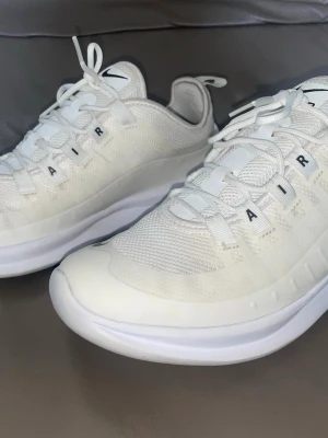 Nike vita Air Max sneakers - Fräscha vita Nike Air Max sneakers med mesh- och syntetmaterial, svarta detaljer och AIR-tryck på snörningen. Skorna har en sportig look med låg profil och klassisk Nike-logga på tungan och framtill. Perfekta för dig som gillar stilrena och bekväma sneakers. Storlek 38.5.