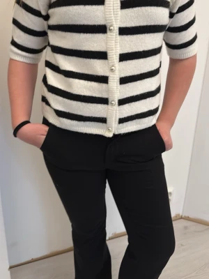Vit och svart randig kofta Kappahl - Kortärmad kofta från Kappahl i mjukt material. Vit bas med svarta horisontella ränder och silvriga knappar framtill. Perfekt för lager-på-lager och enkel att styla till olika outfits.