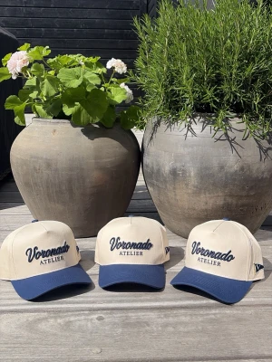 Voronado Rivera Cap - Snygg keps från Voronado Atelier i beige med mörkblå skärm och broderad logga framtill. Klassisk sexpanel-design med justerbar rem bak. Perfekt accessoar för en avslappnad och trendig look.