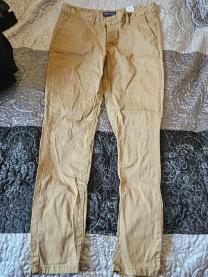 Beige chinos från Pier One - Snygga beige chinos från Pier One med klassisk rak passform och knappgylf. Tillverkade i bomullsmix för skön känsla och stilren look. Perfekta att matcha med en skjorta eller t-shirt för en avslappnad vibe.