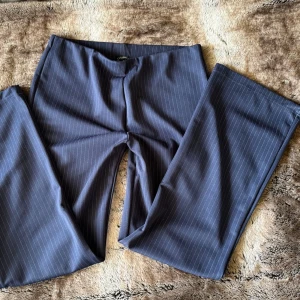 Mörkblå randiga kostymbyxor - Snygga mörkblå kostymbyxor med tunna vita kritstrecksränder från Fashion. Byxorna har rak passform och klassisk midja, perfekta för en stilren look. Materialet känns mjukt och följsamt, vilket gör dem bekväma att bära hela dagen.