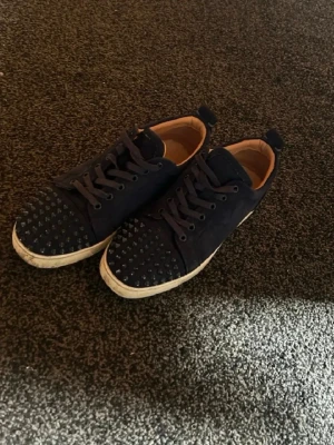 Mörkblå Louboutin sneakers - Snygga mörkblå sneakers med vita sulor och coolt mönster på tån. Skorna har klassisk snörning och är tillverkade i mockaliknande material. Insidan är ljusbrun och de har en enkel, stilren design som passar till det mesta.