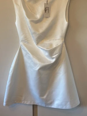 Vit satin kortklänning från Odd muse - Säljer en elegant vit kort klänning från Od muse i satin med rak halsringning och ärmlös design. Klänningen har en stilren och figurnära passform som ger en lyxig känsla. Perfekt för dig som vill sticka ut med en enkel men snygg look.