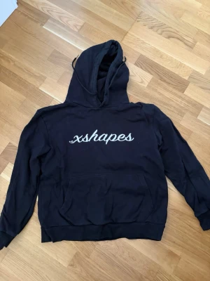 Xshapes hoodies i rosa och svart - Två hoodies från Xshapes, en i ljusrosa och en i svart. Båda har huva med dragsko, stor magficka och tryckt Xshapes-logga på bröstet. Perfekta för en chill och avslappnad stil. Materialet känns mjukt och skönt mot huden.