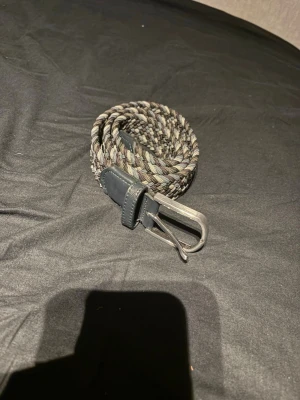 Flätat bälte från Onewear Sweden - Snyggt flätat bälte från Onewear Sweden i flera jordnära färger som svart, grå och beige. Bältet har detaljer i svart skinn och ett klassiskt metallspänne. Perfekt accessoar för att lyfta din outfit.