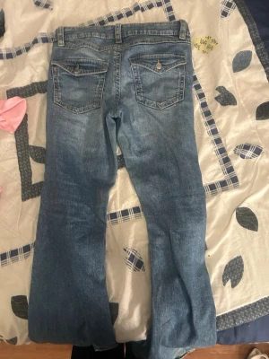 Blå bootcut jeans från Gina Tricot - Säljer ett par ljusblå bootcut jeans från Gina Tricot i storlek 164. Jeansen har klassisk femficksdesign, snygga bakfickor med lock och knapp samt slitningar för en avslappnad look. Tillverkade i mjuk denim med skön stretch.