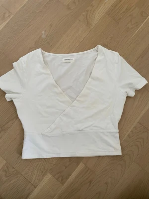 Vit omlottopp från Even&Odd - Snygg vit omlottopp från Even&Odd med korta ärmar och v-ringad hals. Toppen är croppad och har en stilren design som passar perfekt till jeans eller kjol. Tillverkad i mjuk bomull för en bekväm känsla.