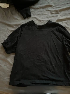 Svart basic t-shirt i bomull - En enkel svart t-shirt i bomull med rund hals och korta ärmar. Perfekt för en clean och avslappnad stil. Passformen är normal och materialet känns mjukt mot huden.