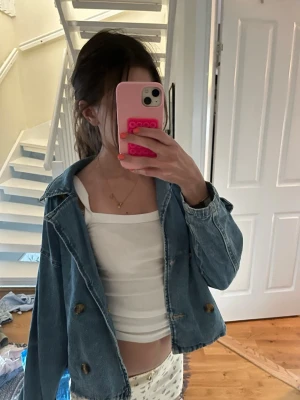 Oversized blå jeansjacka - Snygg oversized jeansjacka i klassisk ljusblå denim med stora bruna knappar och bred krage. Jackan har en avslappnad passform och två fickor framtill. Perfekt att slänga över en t-shirt för en cool look.STORLEK ÄR 152 men känns som en xxs