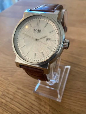 Hugo Boss Dress 42mm Herrklocka - Säljer en snygg herrklocka från Hugo Boss i använt skick enligt bilder. Säljes otestad. Går med fungerande batteri, repor finns, läderarmband behöver bytas, datumvisare, mineralglas, japanskt urverk, vattentät, tachymeter osv.  Nypris: 4000 SEK Mitt pris: 389 SEK  Skickas snabbt och spårbart. Skriv vid frågor och se gärna mina andra annonser!  Model overview Brand Hugo Boss Ref. No. 1512380 RRP 405 Category Classic Style Men's watch, dress watch Warranty 2 years Retailer Warranty Water resistanc