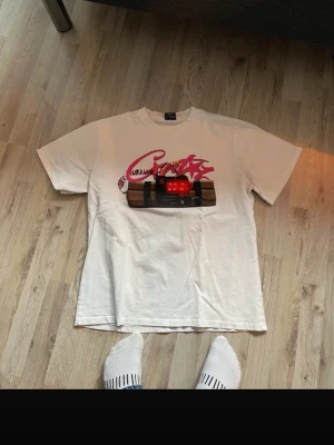 Vit t-shirt med grafiskt tryck - Vit t-shirt från corteiz med ett stort grafiskt tryck på bröstet som föreställer en rosa graffiti-liknande text och en digital klocka. Klassisk passform och rund halsringning. Har även text på ryggen ”NOTIME4LOVE” Perfekt för dig som gillar streetwear och unika prints.